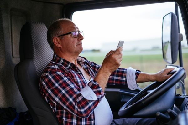 A commercial truck driver looking at a smartphone while behind the wheel, illustrating a high-stakes form of negligence that an Athens, TX, personal injury lawyer handles.